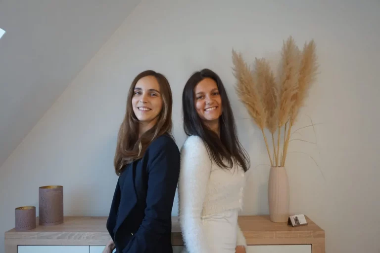Julia und Jacky – Gründerinnen der Feelgood Academy, stehen Rücken an Rücken und lächeln, Symbol für Vertrauen, Teamgeist und Kompetenz