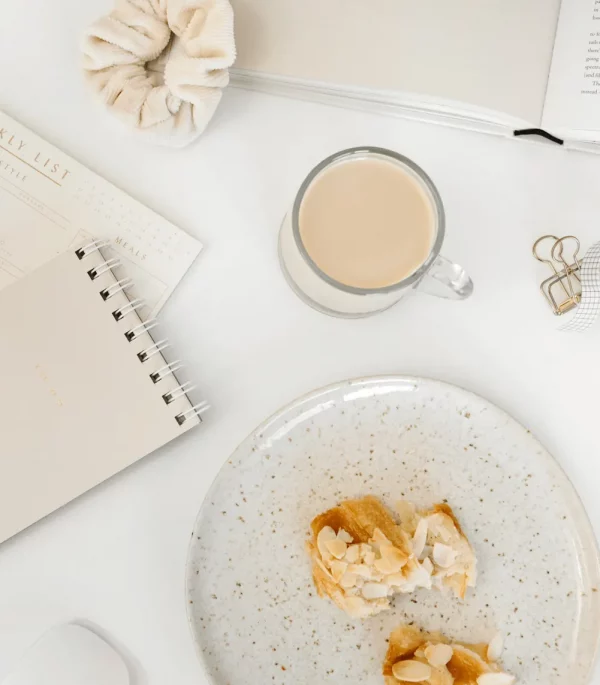 Notizbuch, Kaffee und Teller auf hellem Tisch – Symbol für Fokus, Klarheit und Lernfreude während der Ausbildungen der Feelgood Academy.